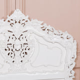 Decorative white headboard with intricate carvings against a pink wall.