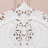 Close-up of an ornate white decorative wall piece against a pink background