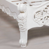 Close-up of a white ornate chair leg on a light wooden floor.