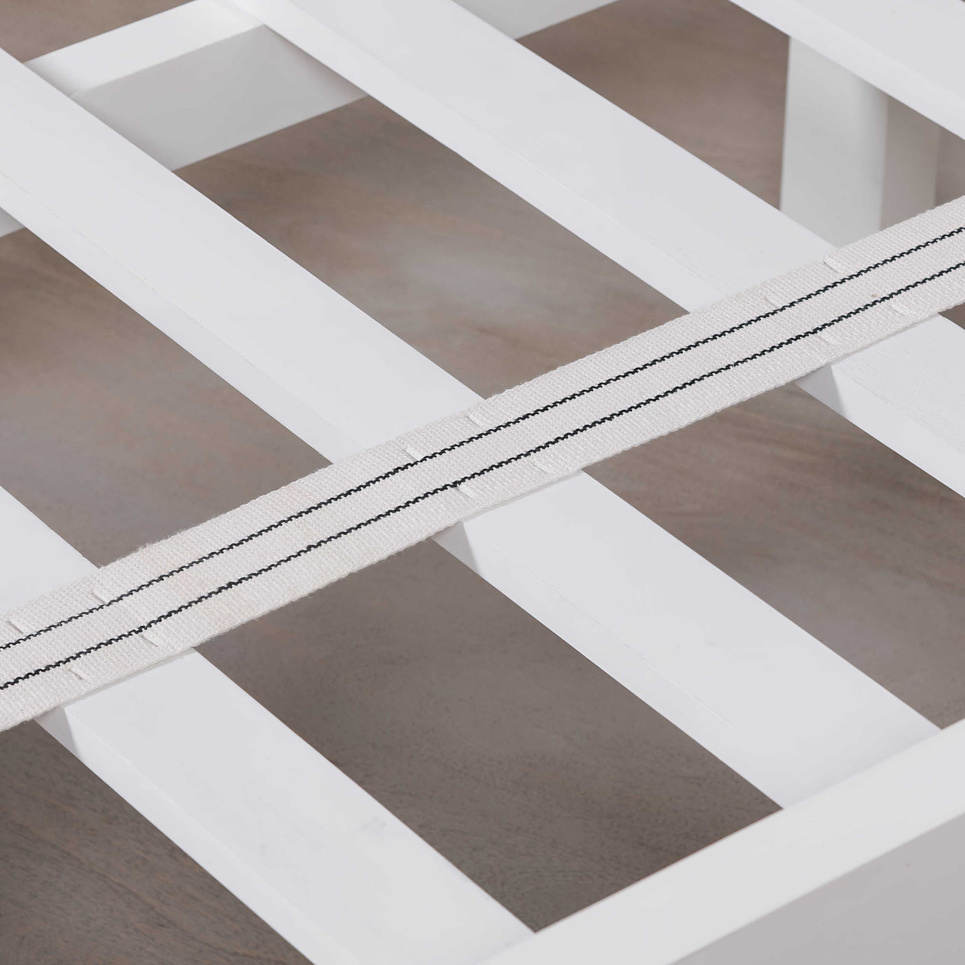 Close-up of a white wooden bed frame on a wooden floor.