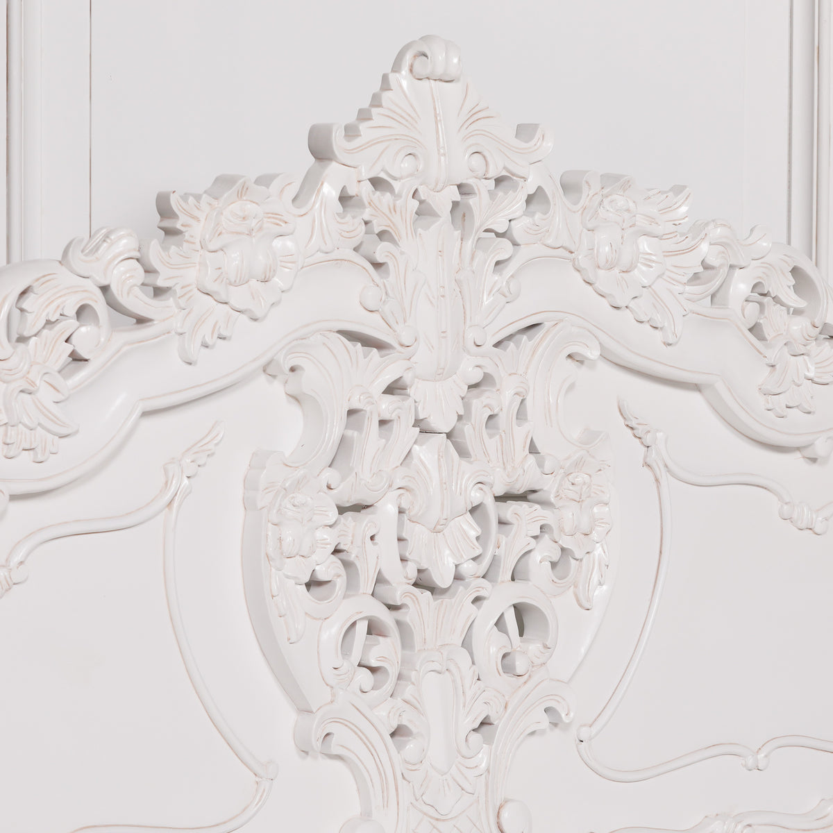 Close-up of an ornate white carved headboard with intricate floral and scrollwork details against a matching white background.