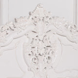 Close-up of an ornate white carved headboard with intricate floral and scrollwork details against a matching white background.