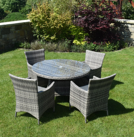 Rattan outdoor dining set with round glass table and four armchairs on garden lawn