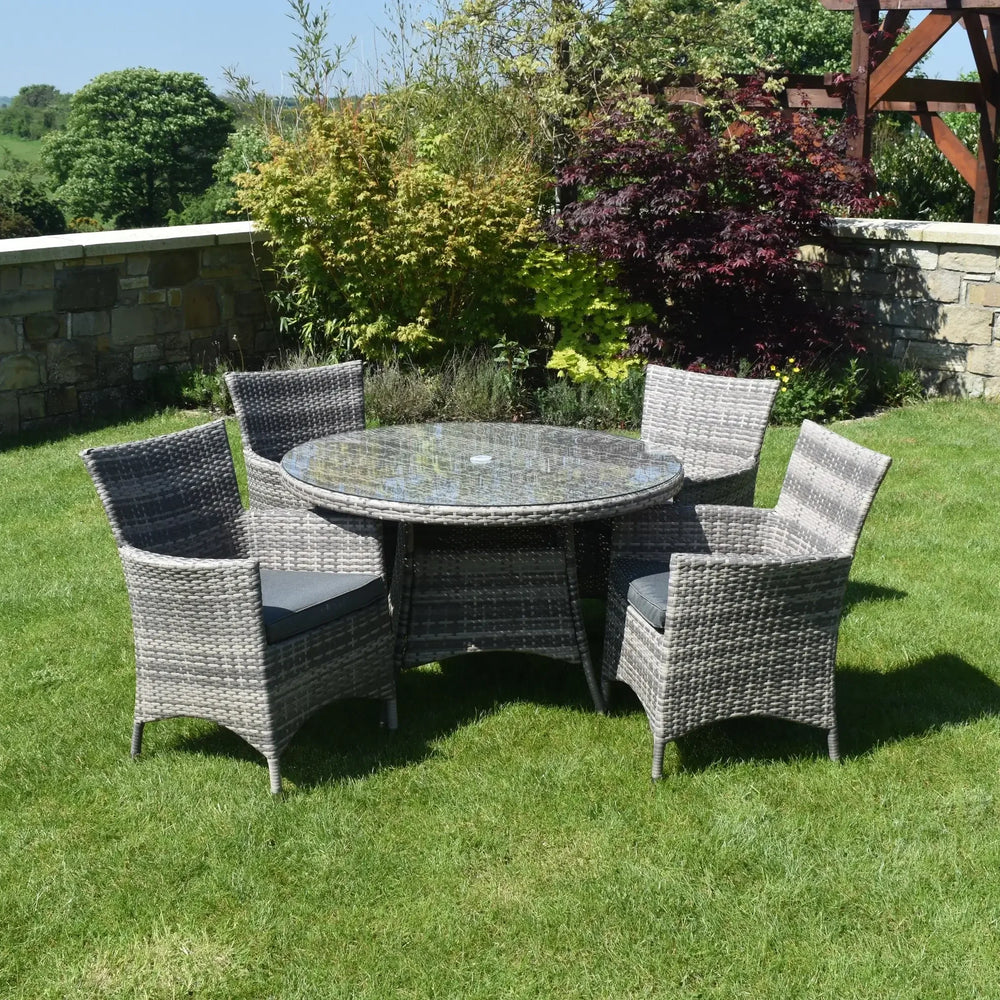 Grey rattan dining set with glass top table and five chairs on lawn in garden setting