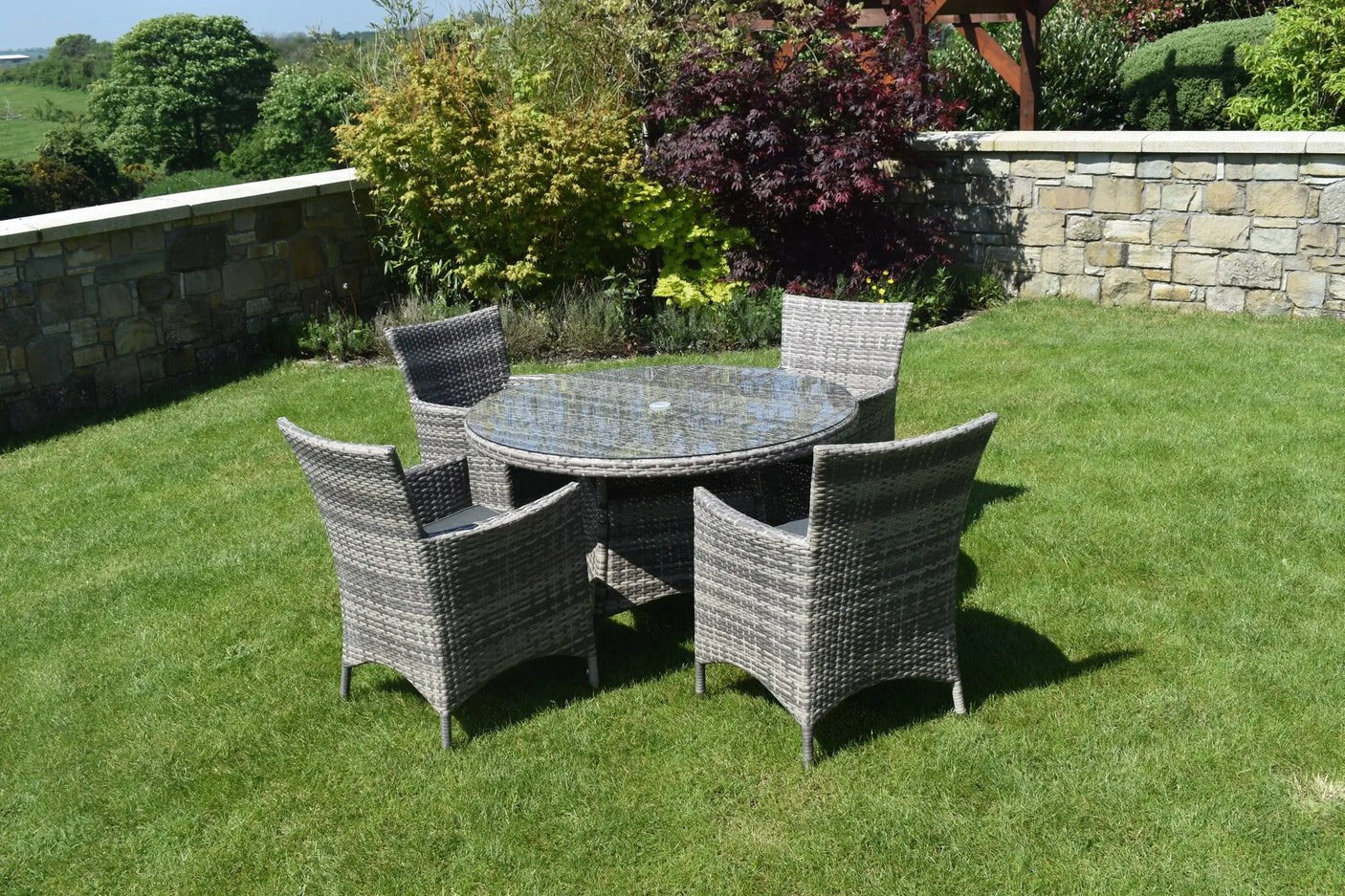 Grey rattan dining set with round glass table and four chairs on garden lawn