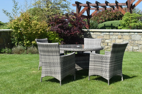 Rattan dining set with round glass table and four chairs on green lawn