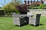 Rattan dining set with round glass table and four chairs on green lawn