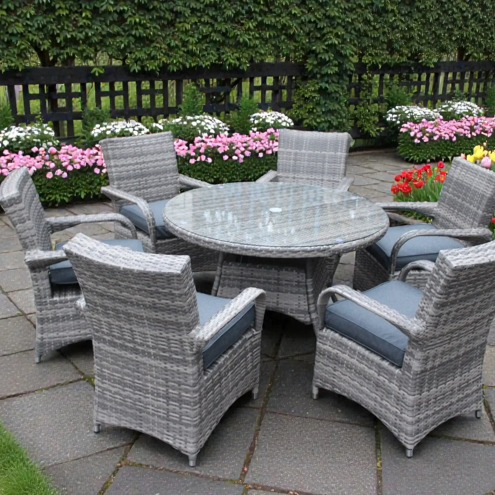 Grey rattan dining set with glass round table and six cushioned chairs on garden patio
