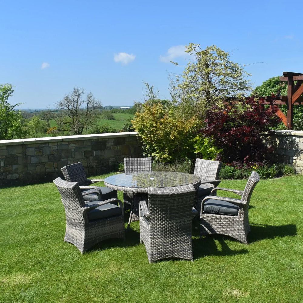 Rattan outdoor dining set with glass top table and six cushioned chairs on garden lawn