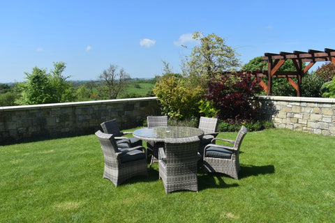 Rattan outdoor dining set with glass top table and six cushioned chairs on garden lawn