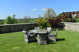 Rattan outdoor dining set with glass top table and six cushioned chairs on garden lawn