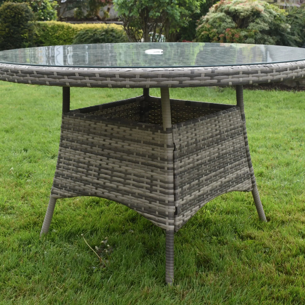 Round rattan outdoor dining table with glass top on grass garden lawn