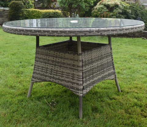 Round rattan outdoor dining table with glass top on grass garden lawn