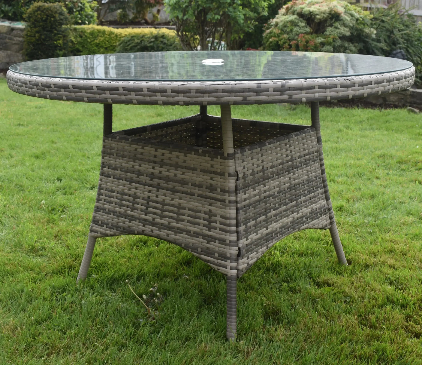 Round rattan outdoor dining table with glass top on grass garden lawn