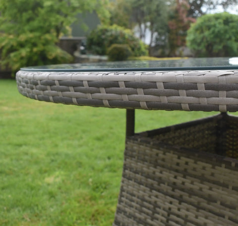 Close-up of rattan outdoor dining table with glass top on lawn