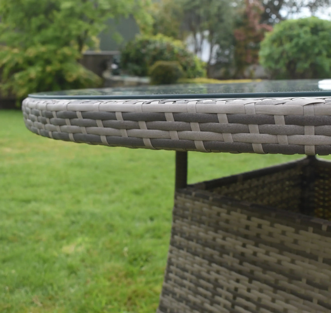 Close-up of rattan outdoor dining table with glass top on lawn