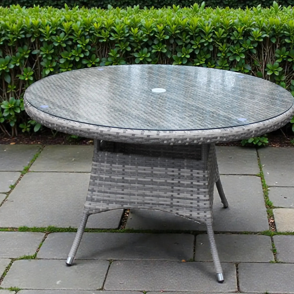 Round rattan outdoor dining table with glass top on stone patio