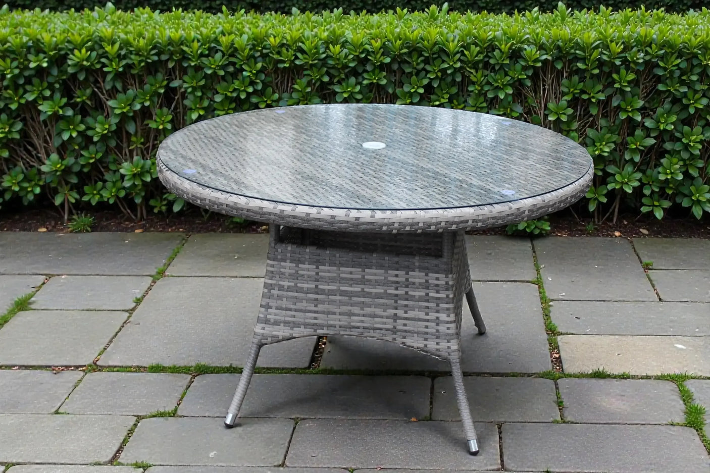Round rattan outdoor dining table with glass top on stone patio