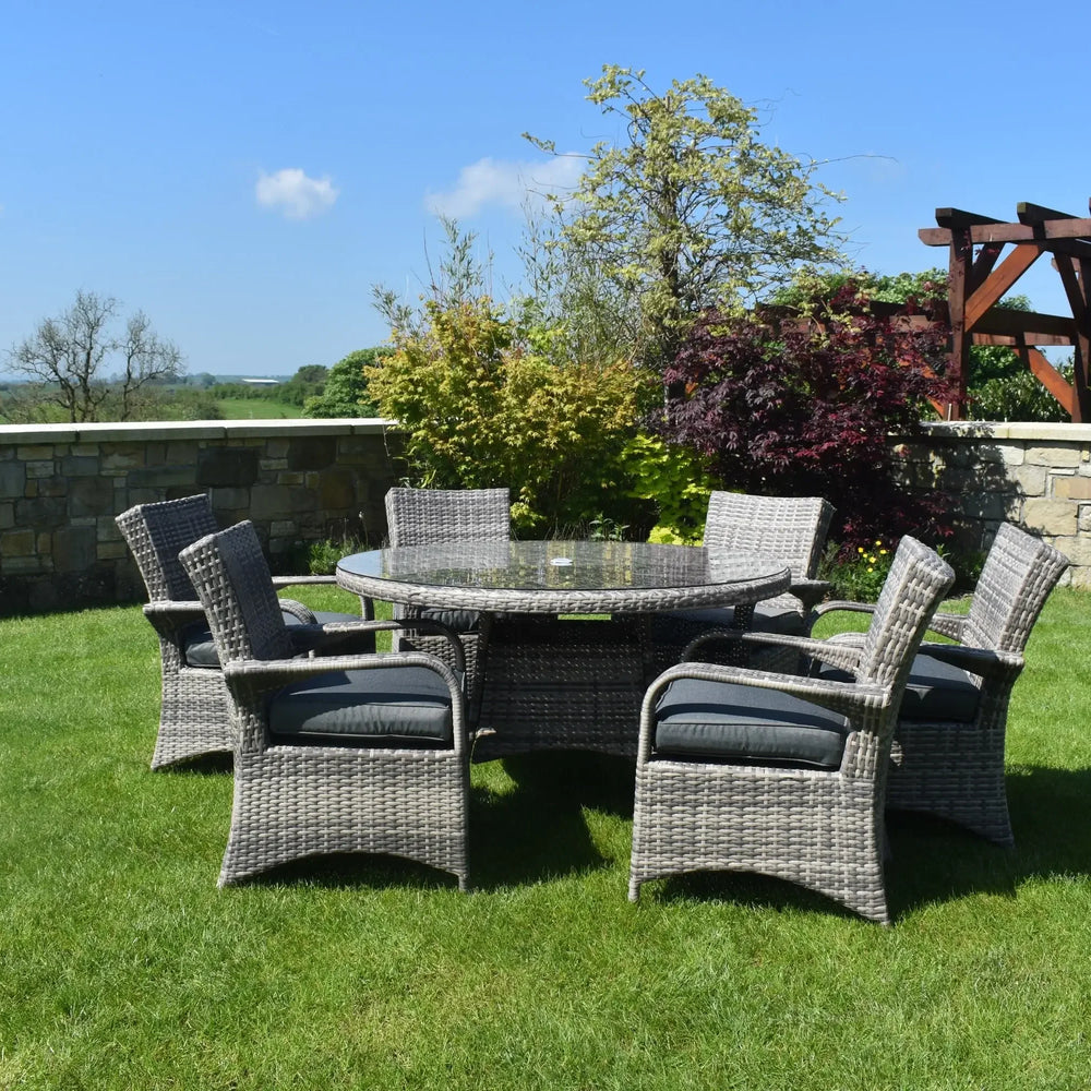Grey rattan dining set with six cushioned chairs and round glass table on a garden lawn
