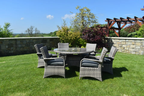 Grey rattan dining set with six cushioned chairs and round glass table on a garden lawn