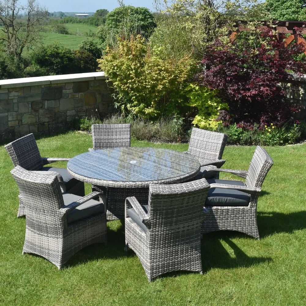 Grey rattan dining set with round glass-top table and six chairs on garden lawn
