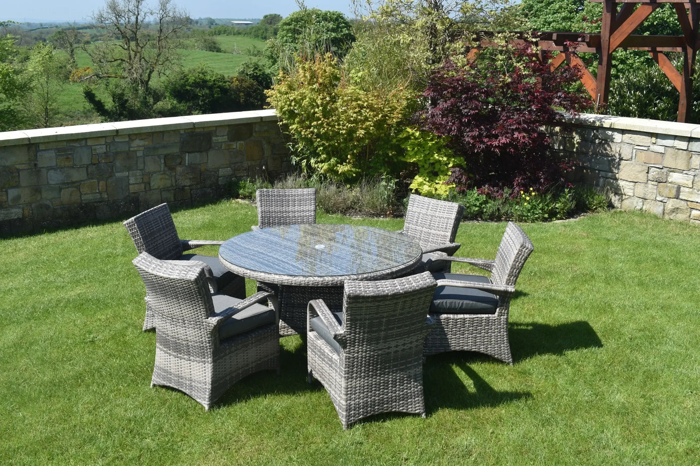 Grey rattan dining set with round glass-top table and six chairs on garden lawn