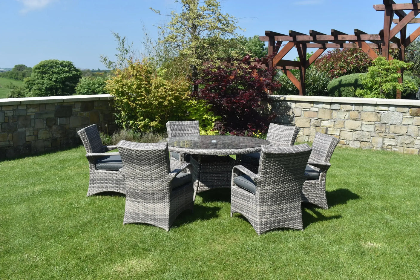 Grey rattan garden dining set with six armchairs and round glass table on lawn