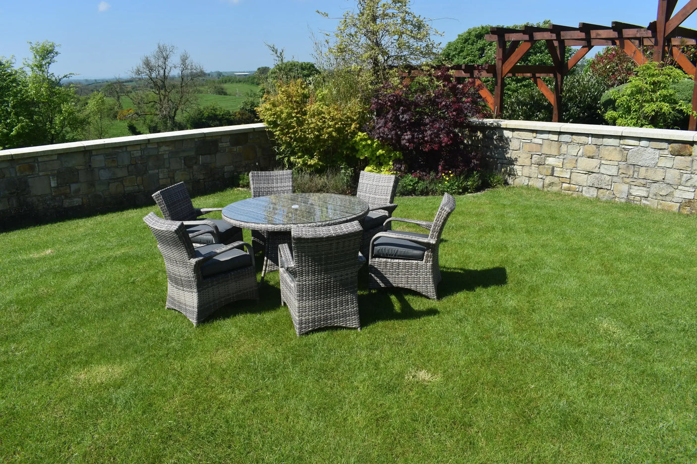 Rattan dining set with glass table and six cushioned chairs on patio lawn