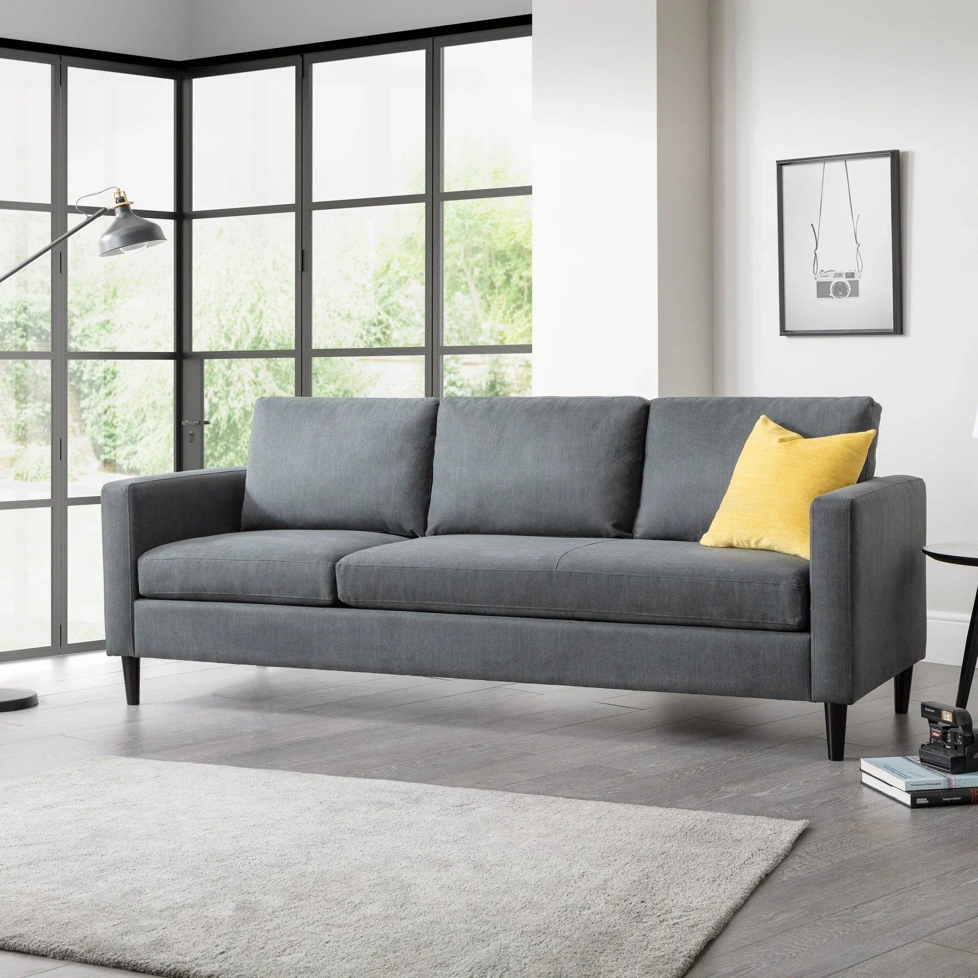Grey corner sofa with yellow cushion in bright living room with large windows and rug
