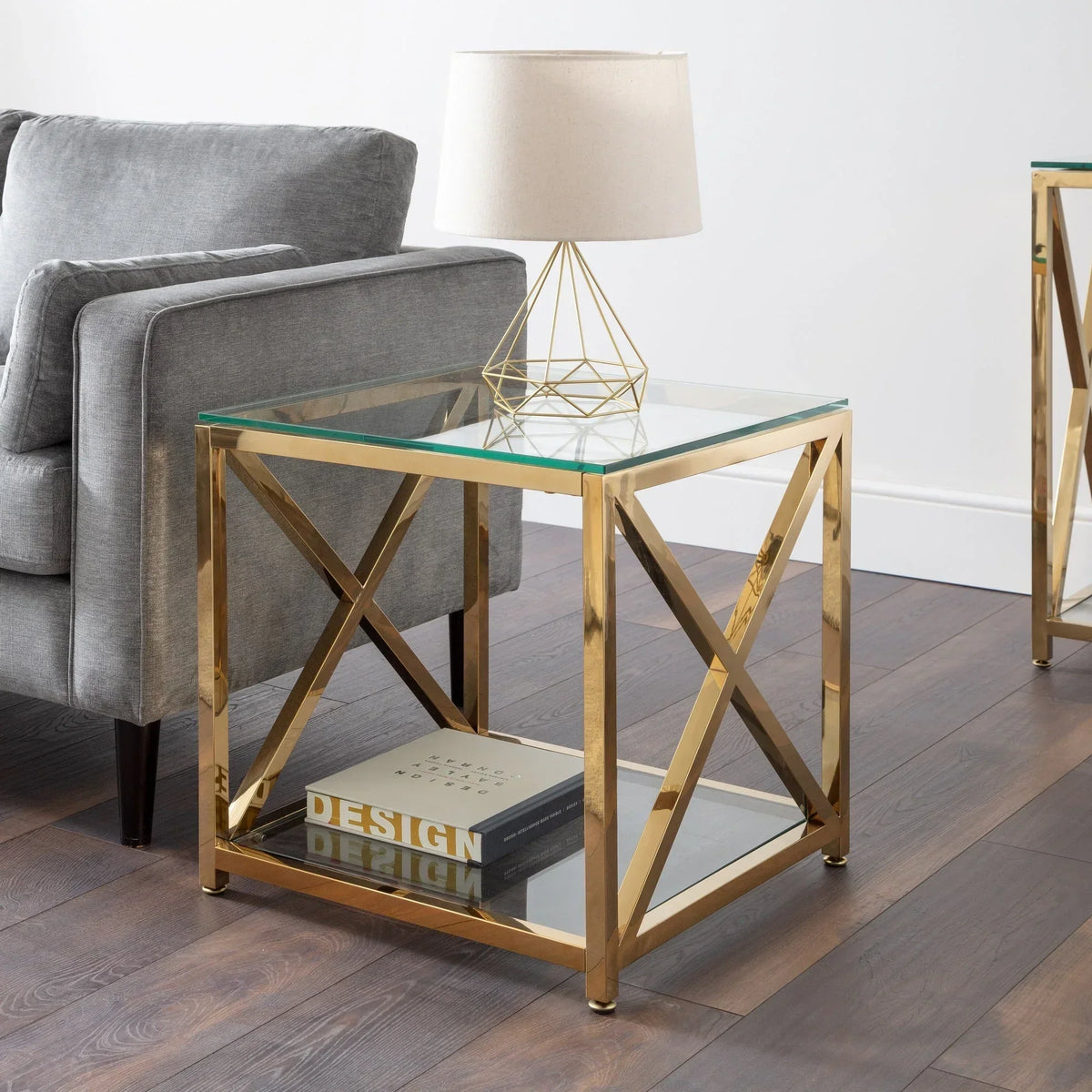 Gold lamp table with glass top beside grey sofa on wooden floor