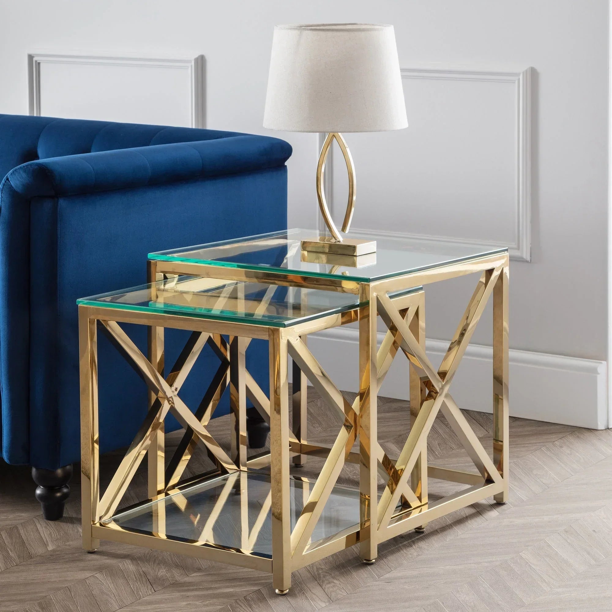 Gold nest of tables with glass tops beside blue sofa, topped with cream table lamp