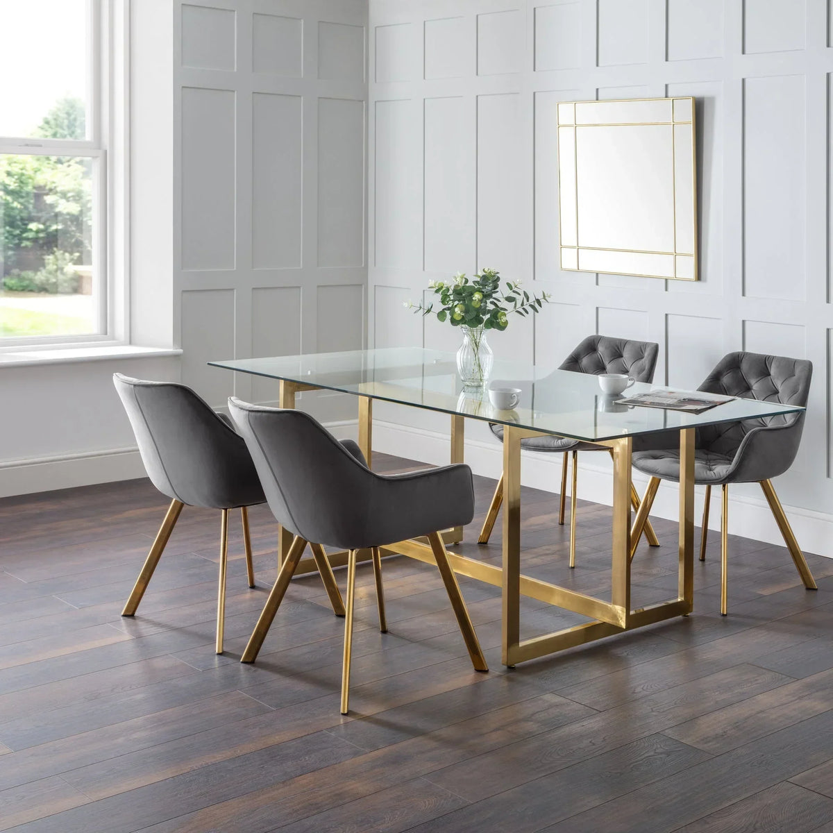 Glass dining table with gold legs and four grey velvet chairs in modern dining room