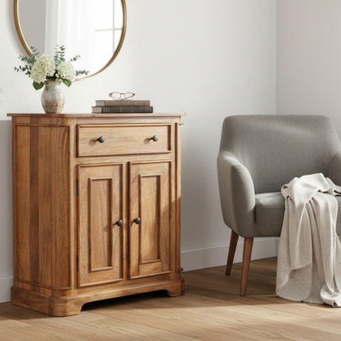 Wooden cabinet next to a gray chair in a room with a round mirror and flowers.