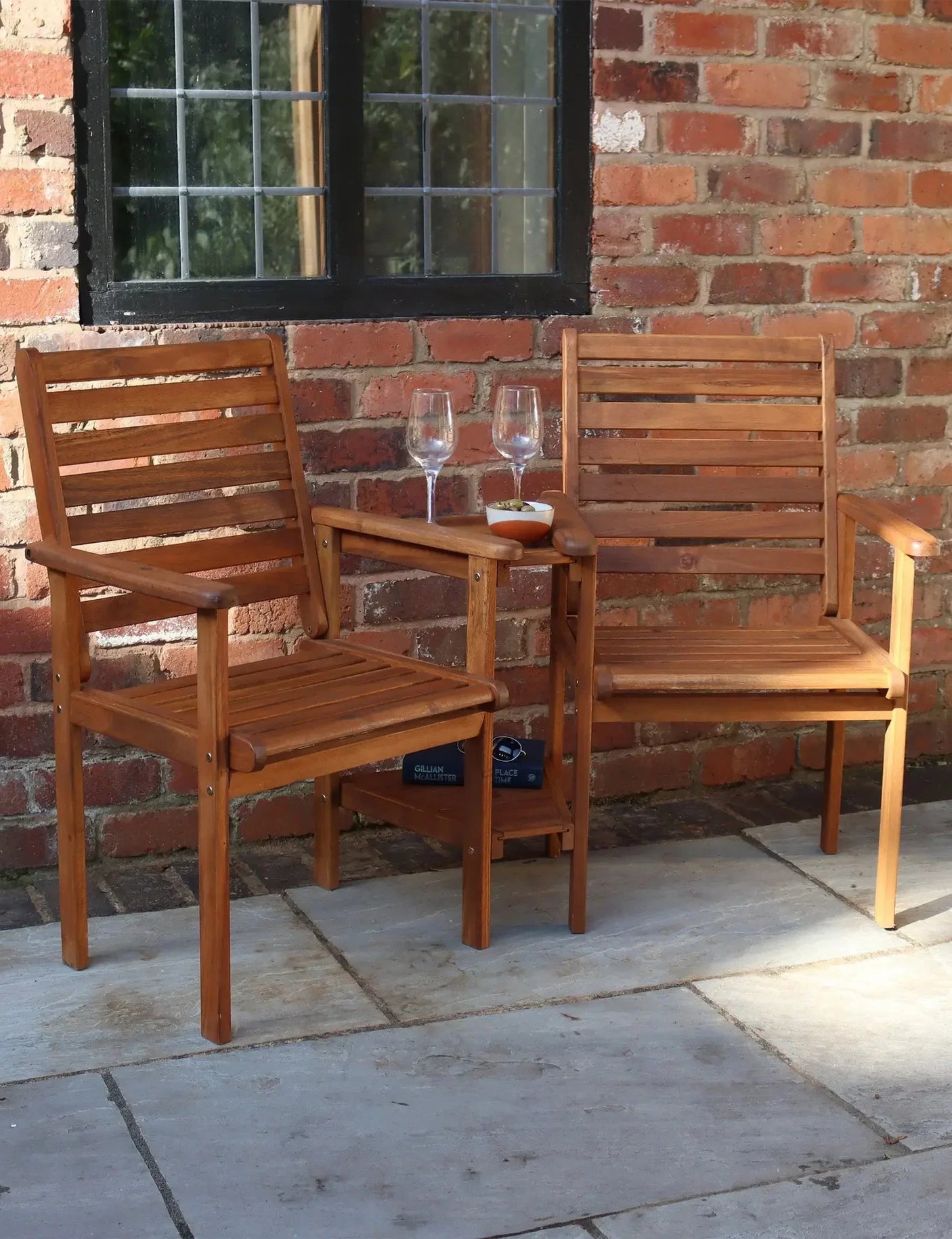 Wooden love seat garden furniture set with built-in table, placed on patio by brick wall