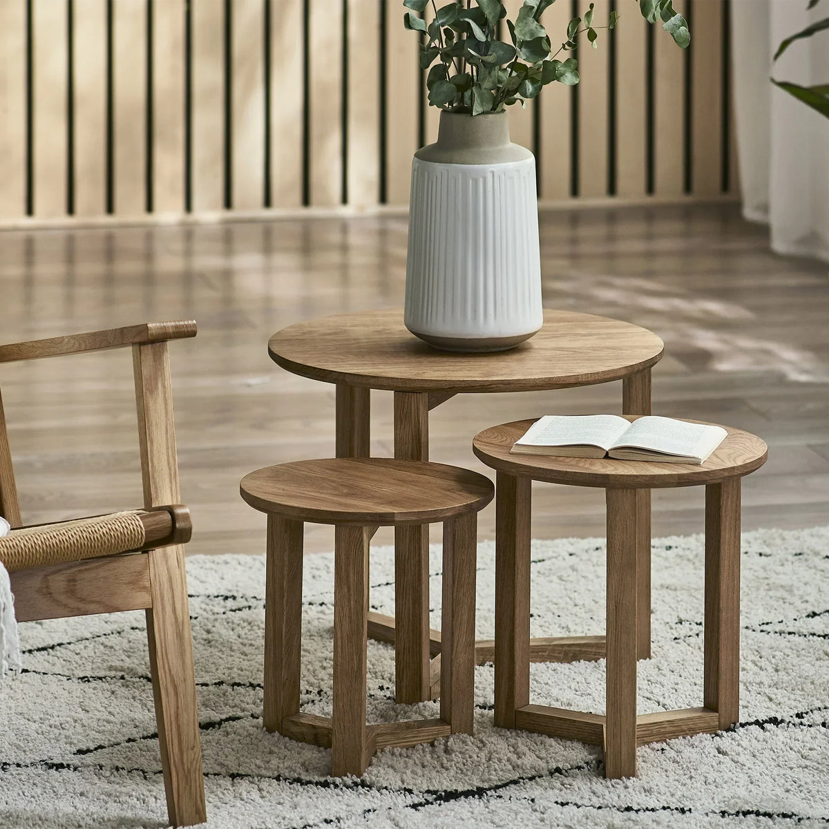 Oak nest of tables set on patterned rug with ceramic vase and open book