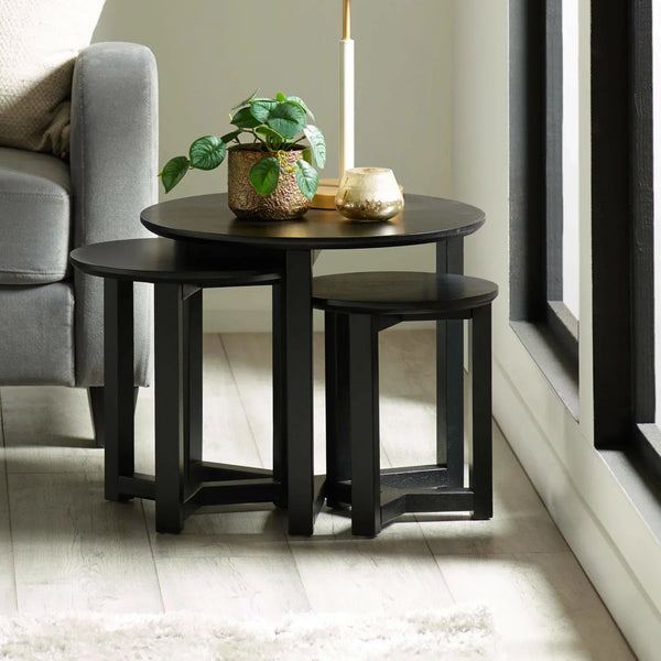Black wooden nesting tables with plant and candle beside grey sofa on wood floor