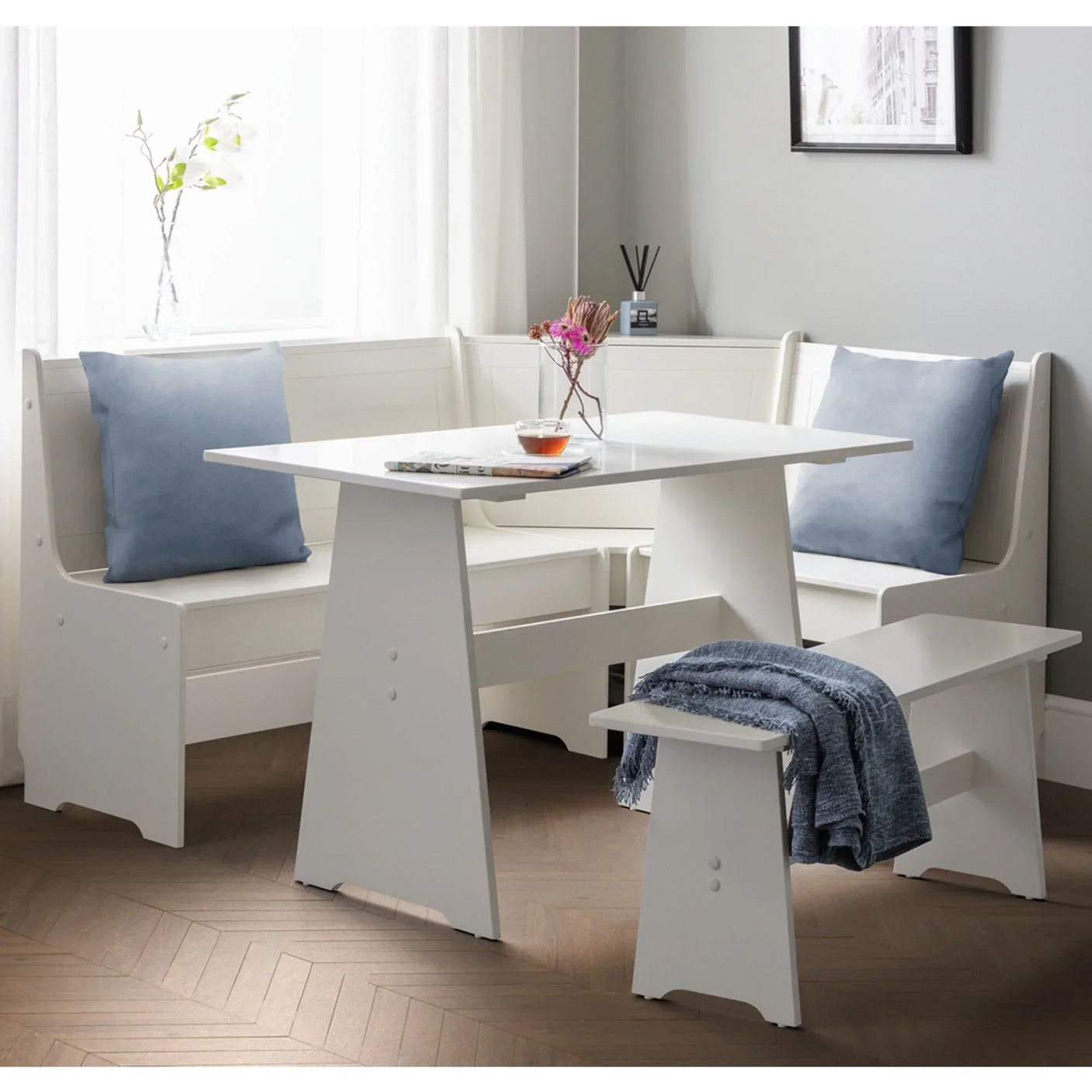 White corner dining set with table, benches, blue cushions and blanket in modern room