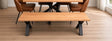 A wooden dining table with a matching bench and brown upholstered chairs in a bright room with light wood flooring.
