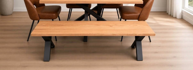 A wooden dining table with a matching bench and brown upholstered chairs in a bright room with light wood flooring.