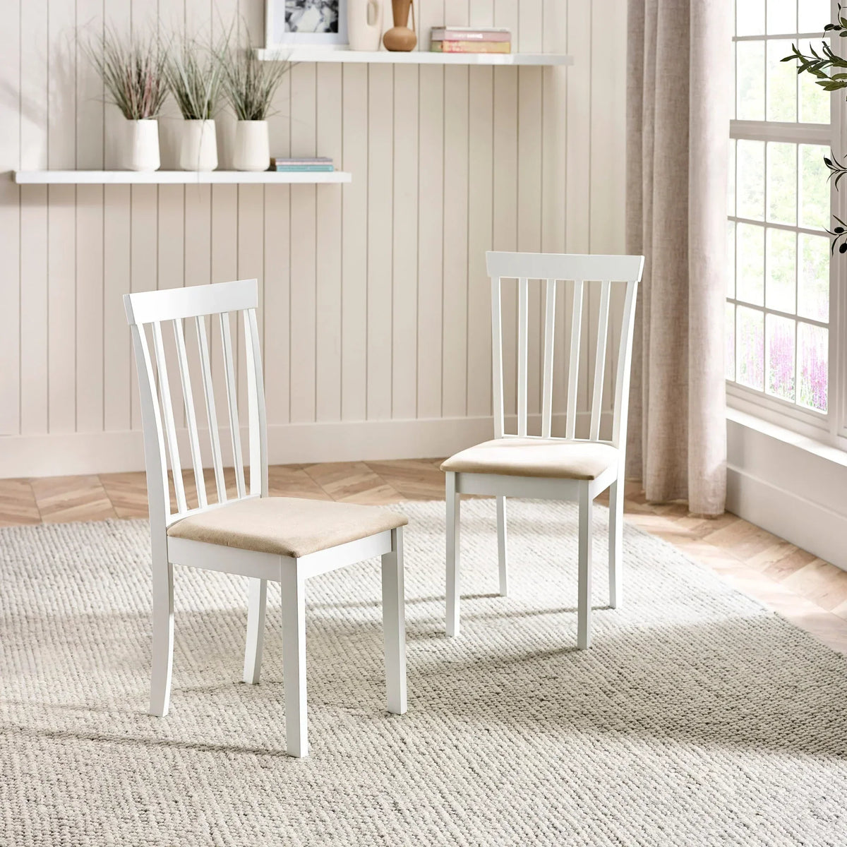 Pair of white wooden dining chairs with beige cushioned seats in bright living room