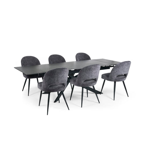 Extended black dining table with six grey velvet upholstered chairs with black legs on white background.