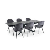 Extended black dining table with six grey velvet upholstered chairs with black legs on white background.