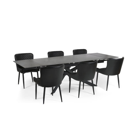 Extended black dining table with six black leather chairs with diamond quilted backrests on white background.