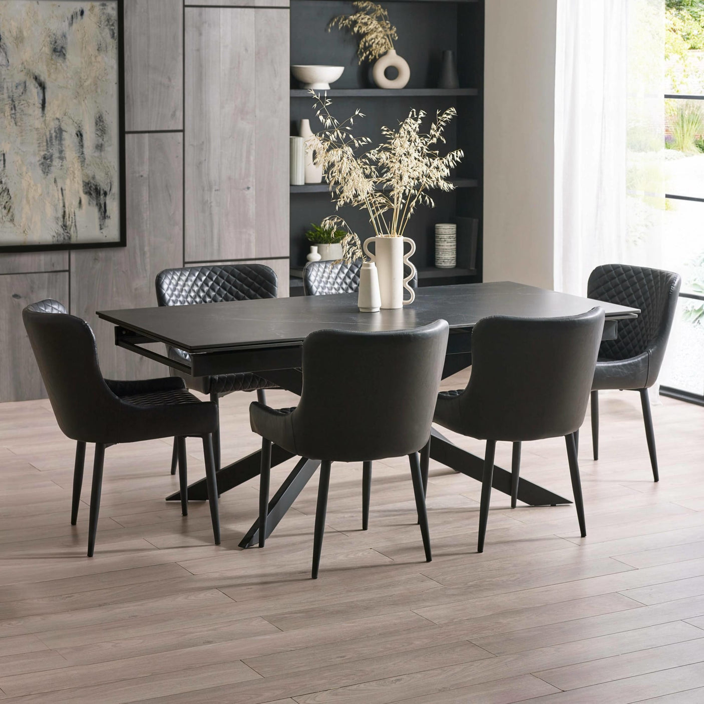Extended black dining table with six black leather chairs, light wood flooring, decorative vases