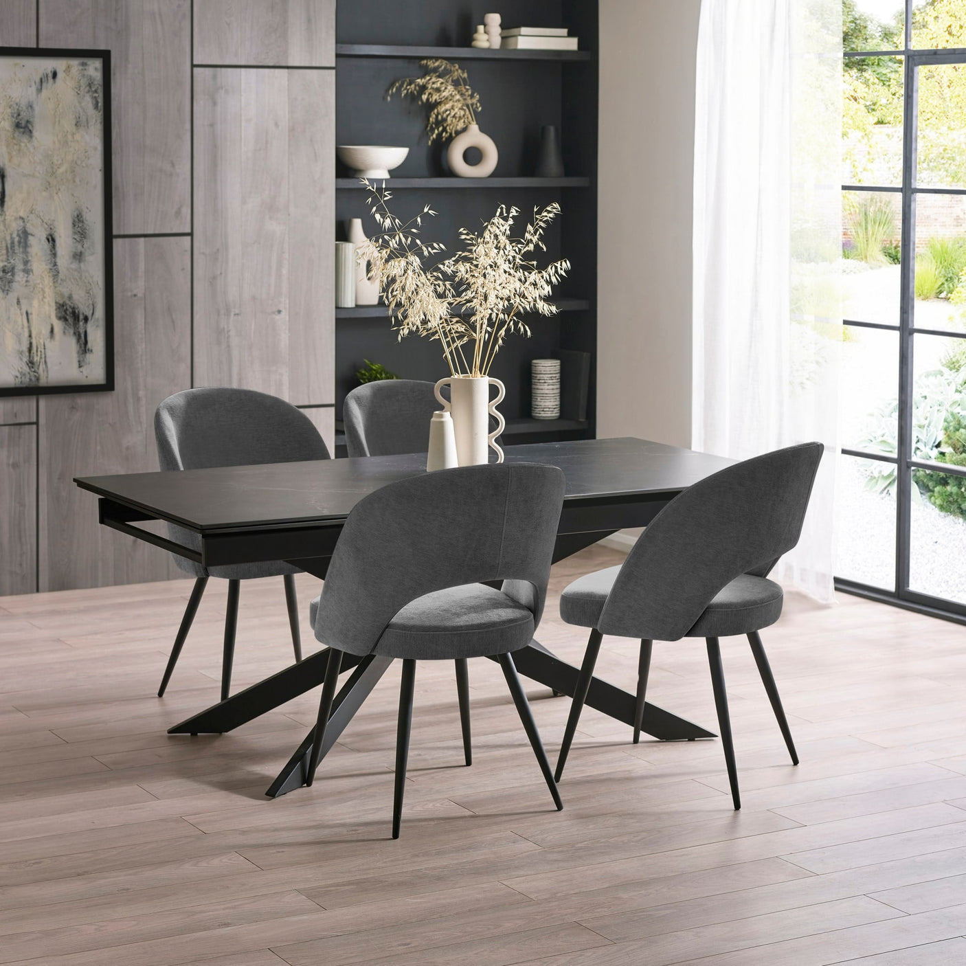 Black dining table with four dark grey fabric chairs, minimalist modern decor, light wood floor