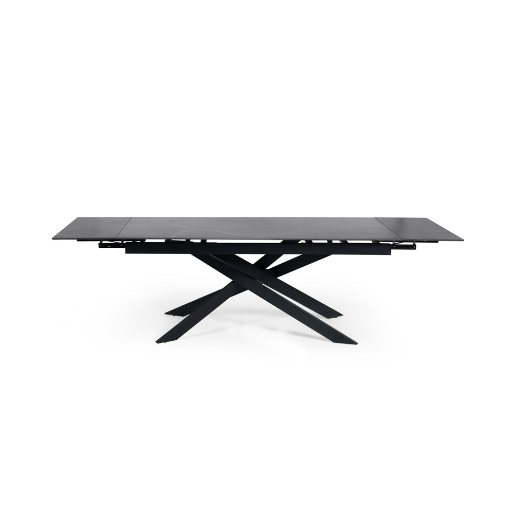 Extended rectangular dining table with black marble top and black metal crossed legs, front view isolated on white