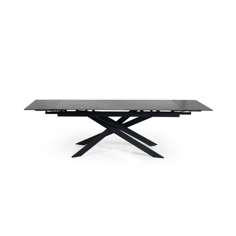 Extended rectangular dining table with black marble top and black metal crossed legs, front view isolated on white
