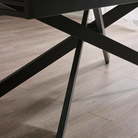 Close-up of black metal crossed legs supporting the table on light wooden floor