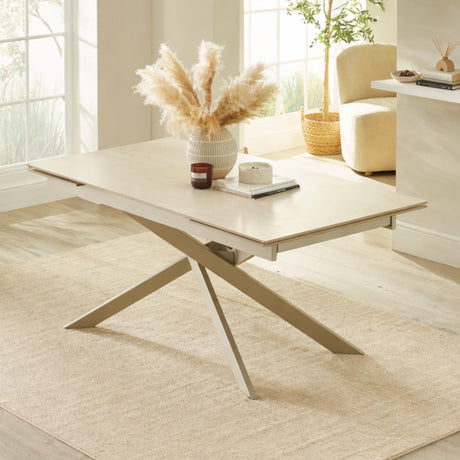 Light beige extending dining table with crossed metal legs in cream, set in bright room on textured beige rug