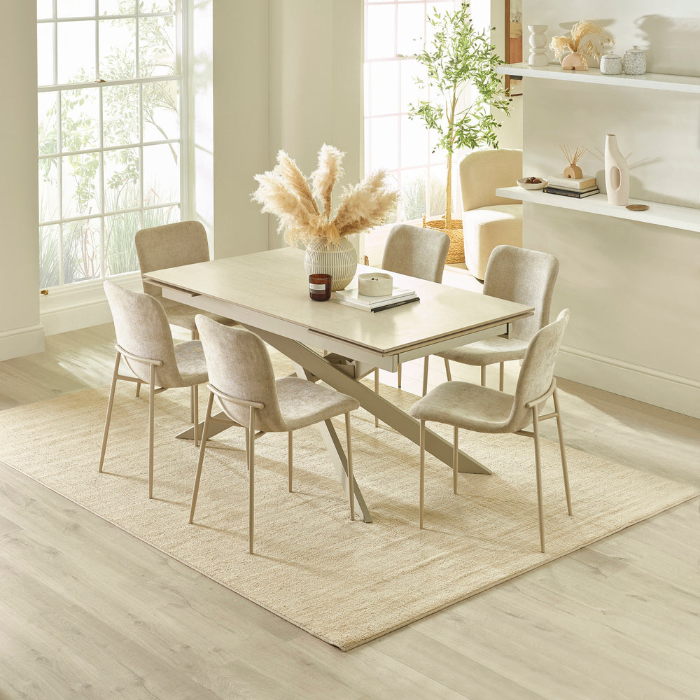 Light beige dining table with six chairs in bright dining room with large windows and decorative vase